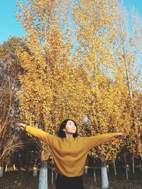 Woman with arms outstretched standing against trees during autumn