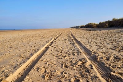 Tire tracks on sand against sky