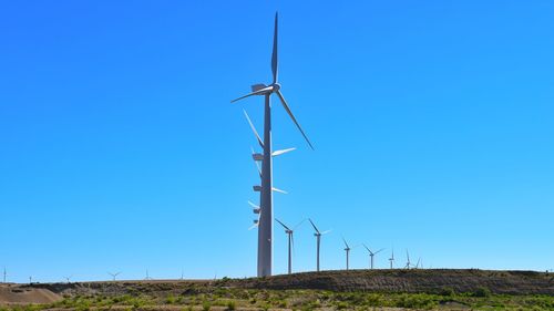 Low angle view of windmill on field against clear blue sky