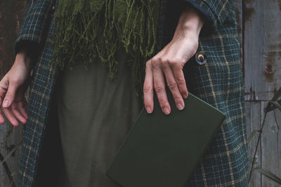 A woman in a dress and coat outdoors holds a book in her hand. no face visible.