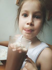 Close-up portrait of girl with iced coffee sitting against wall at home