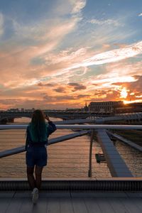 Rear view of woman using phone on bridge over river at sunset