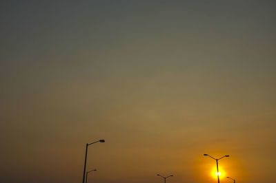 Low angle view of street lights against orange sky