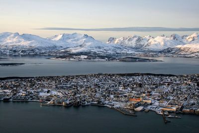 Aerial view of city by sea against snowcapped mountains
