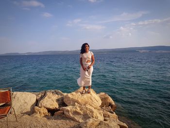 Woman standing on rock by sea against sky