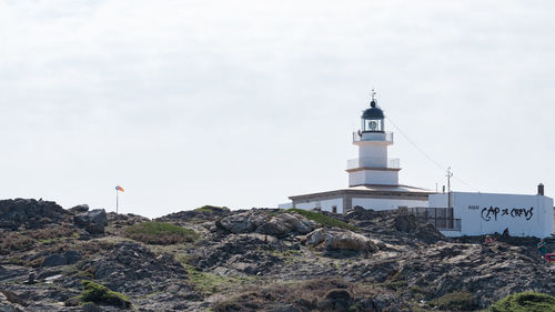 Lighthouse on cliff by sea against sky