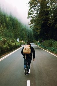 Rear view of male hiker walking on road amidst trees
