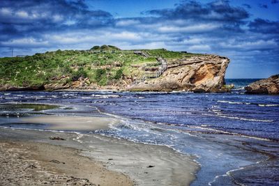 Scenic view of rocky beach against cloudy sky