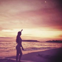 Silhouette woman standing on beach against sky during sunset