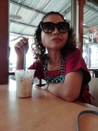 Portrait of woman wearing sunglasses sitting on table at restaurant