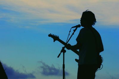 Silhouette musician with guitar against sky