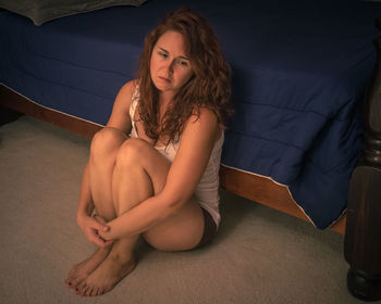 Full length of depressed woman sitting by bed at home