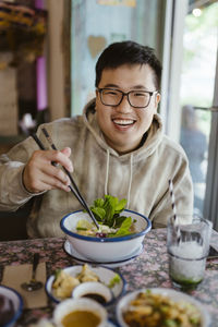 Portrait of smiling young man with food holding chopsticks at restaurant