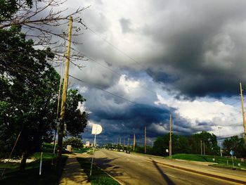 Road by trees against dramatic sky