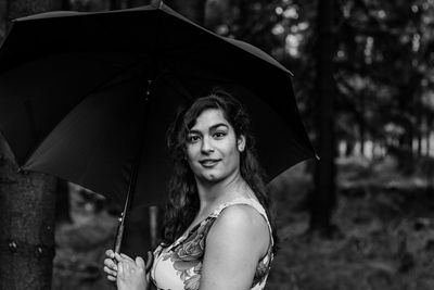 Portrait of smiling young woman with umbrella standing in forest