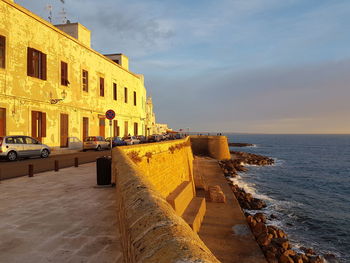 Building by sea against sky during sunset