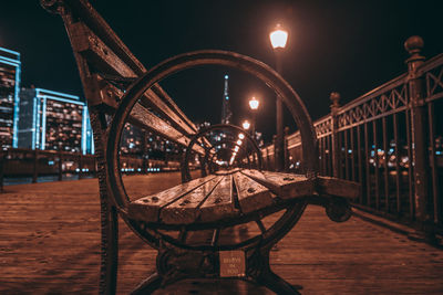 Empty bench on illuminated bridge against sky at night