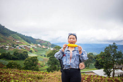 Portrait of woman eating sweetcorn while standing on land against sky