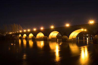 Illuminated bridge over river against sky at night