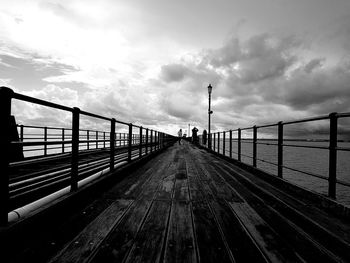 Surface level of pier on calm sea against cloudy sky