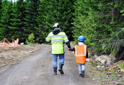 Rear view of father and son wearing reflective clothing while walking in forest