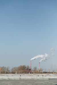 Smoke emitting from factory against clear sky