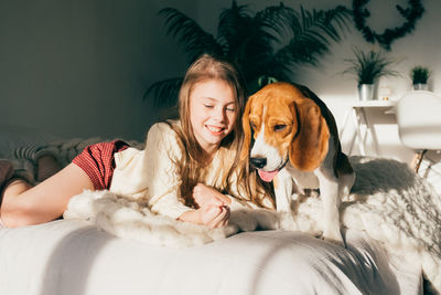 Smiling girl with dog relaxing on bed at home