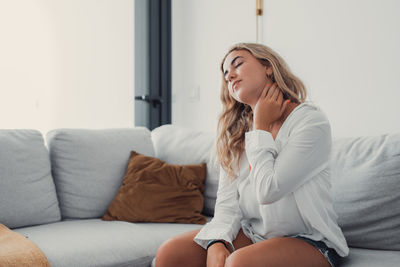 Side view of young woman sitting on sofa at home