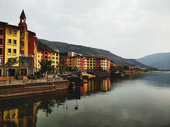 Buildings by lake and mountains against sky