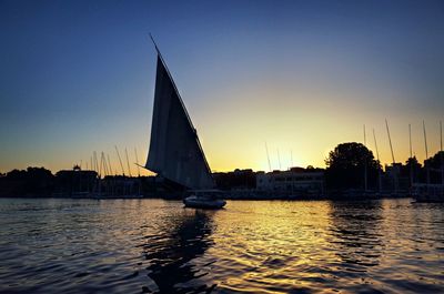 Silhouette sailboat sailing on river against sky during sunset