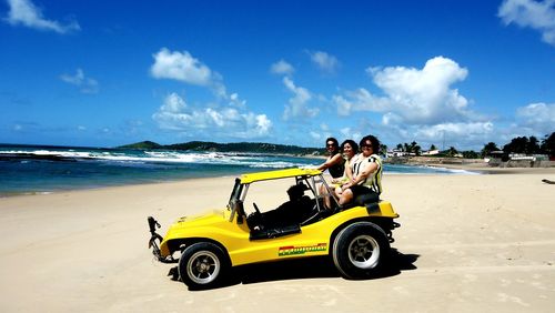 Portrait of smiling friends sitting on buggy at beach against sky