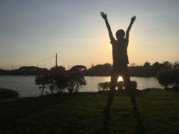 Silhouette person standing at riverbank against sky during sunset