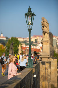 Woman standing on by street light against sky in city