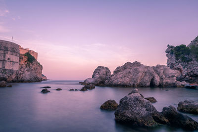 Rocks in sea against sky during sunset