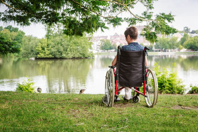 Rear view of man sitting on grass by lake