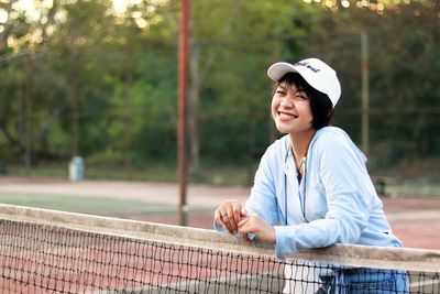 Beautiful asian woman with short hair, wearing hat and smiling broadly on tennis court