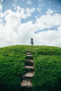 Low angle view of woman standing on grassy hill against sky