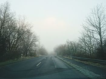 Road amidst trees against sky during winter