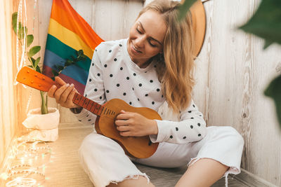 Young millennial hippie woman sitting on balcony play guitar. music lesson and singer sitting. lgbtq 