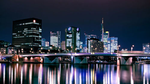 Illuminated buildings by river against sky in city at night