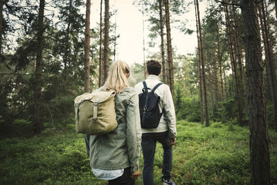 Rear view of couple carrying backpacks while walking through forest