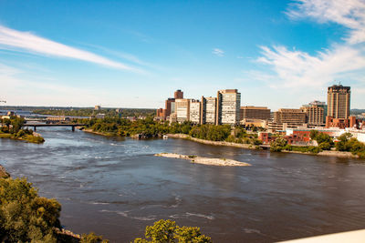 Buildings by river against sky in city
