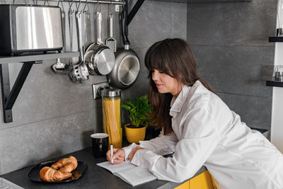 Young attractive woman in white shirt writing in notebook on kitchen counter. portrait of an attract