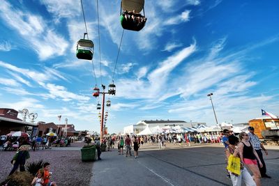 Low angle view of ski lift over road in amusement park ride against cloudy sky