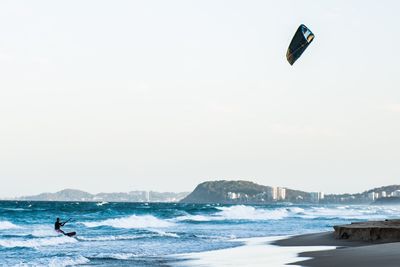 Person paragliding on beach against sky