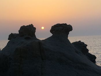 Silhouette rocks on shore against sky during sunset