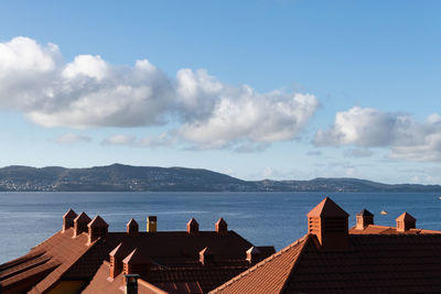 People looking at sea by buildings against sky