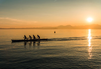 Silhouette people standing on sea against sky during sunset