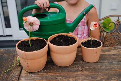 Midsection of girl with watering can by potted plant
