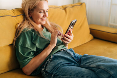 Young woman using mobile phone while sitting on bed at home